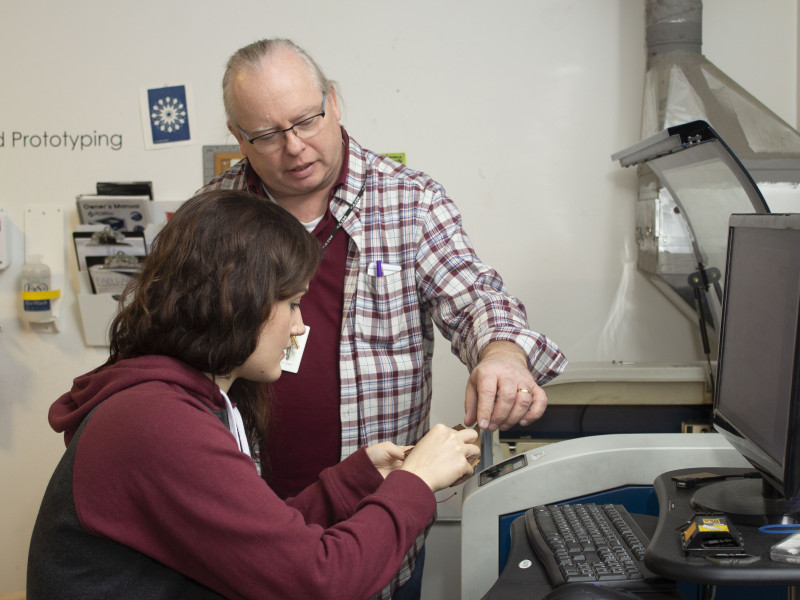 Instructor Joe Chase works with student Sarah Leclair to create a 3D object using a laser cutter.