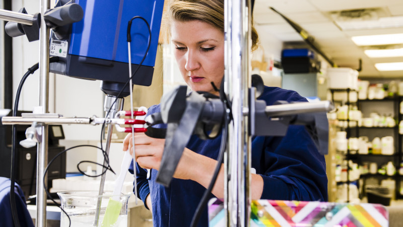 Woman stirs contents of beaker in lab setting