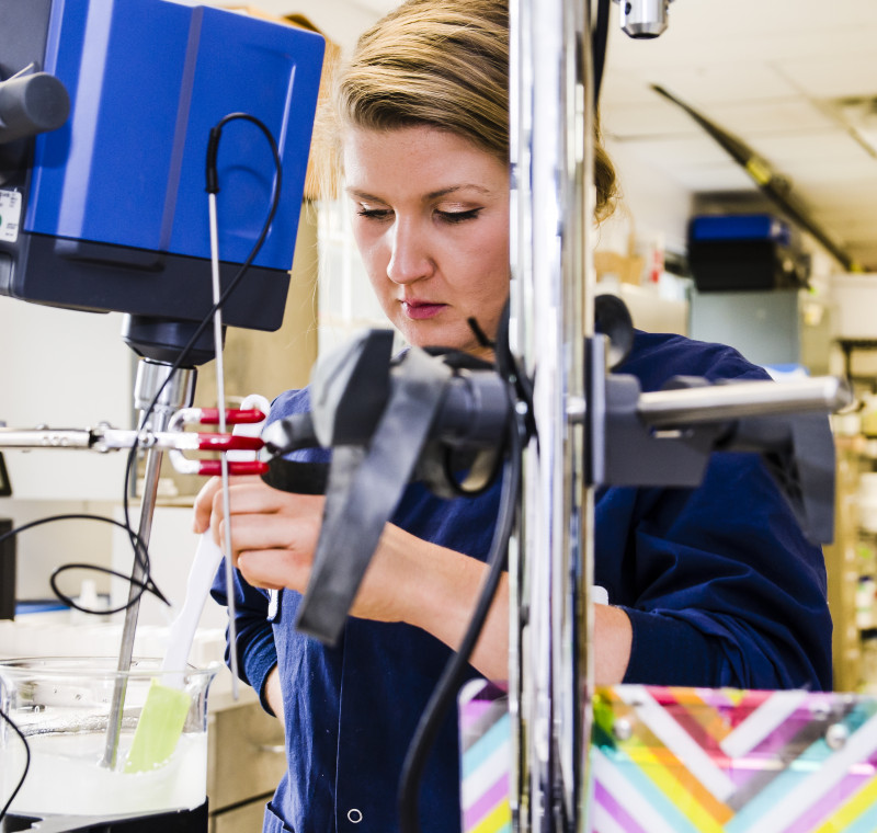 Woman stirs contents of beaker in lab setting