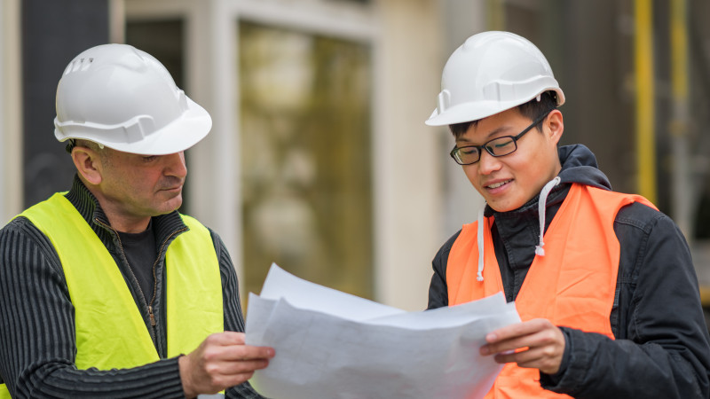 Construction worker and intern look at a paper